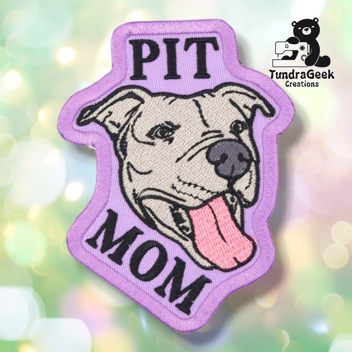Lavender embroidered patch with a purple merrowed edge, showing the same smiling full-eared pitbull with its tongue out. "PIT" is stitched above the dog's head and "MOM" below, both in black block lettering.