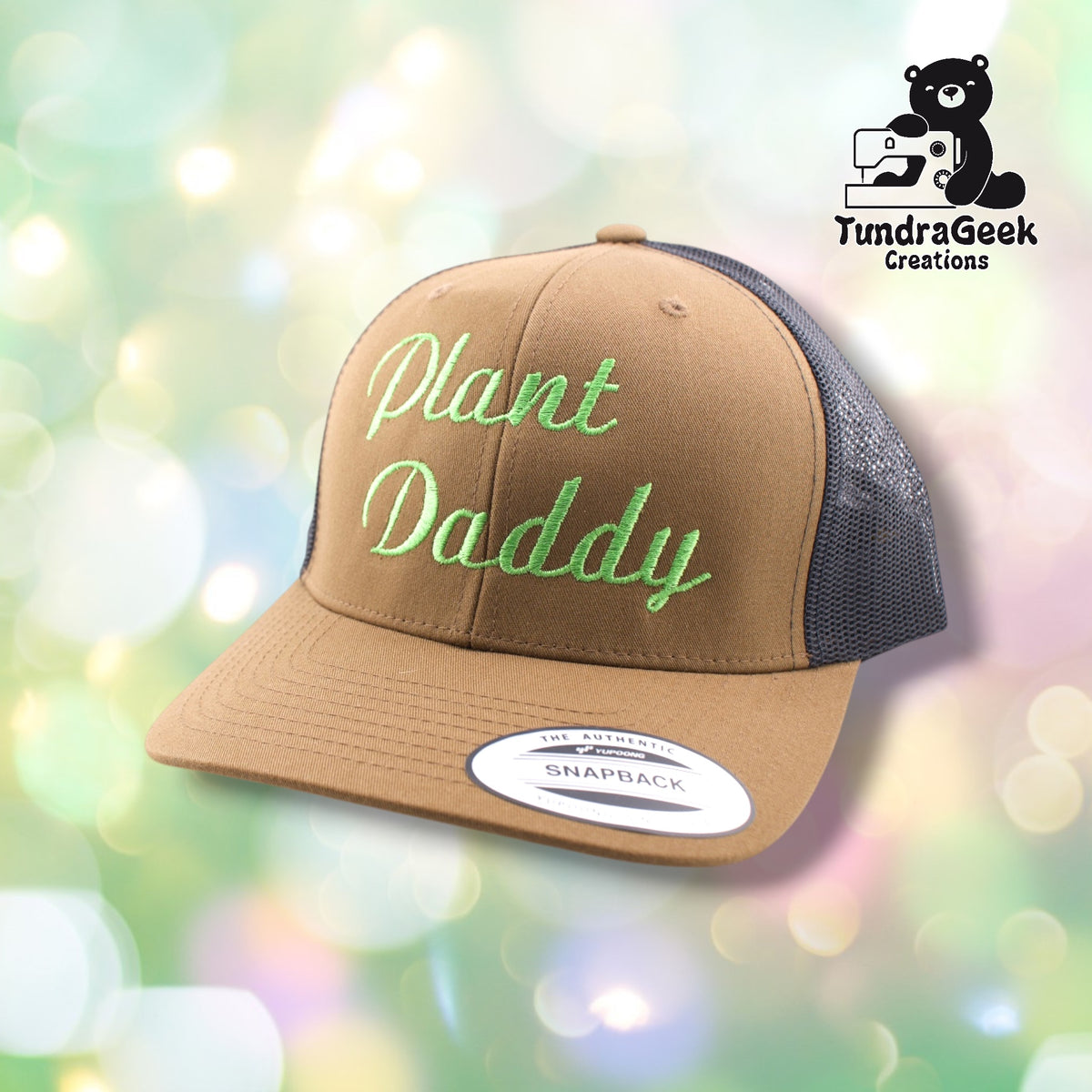 A tan and black trucker snapback hat with green embroidered "Plant Daddy" text on a soft-focus green and white bokeh background.