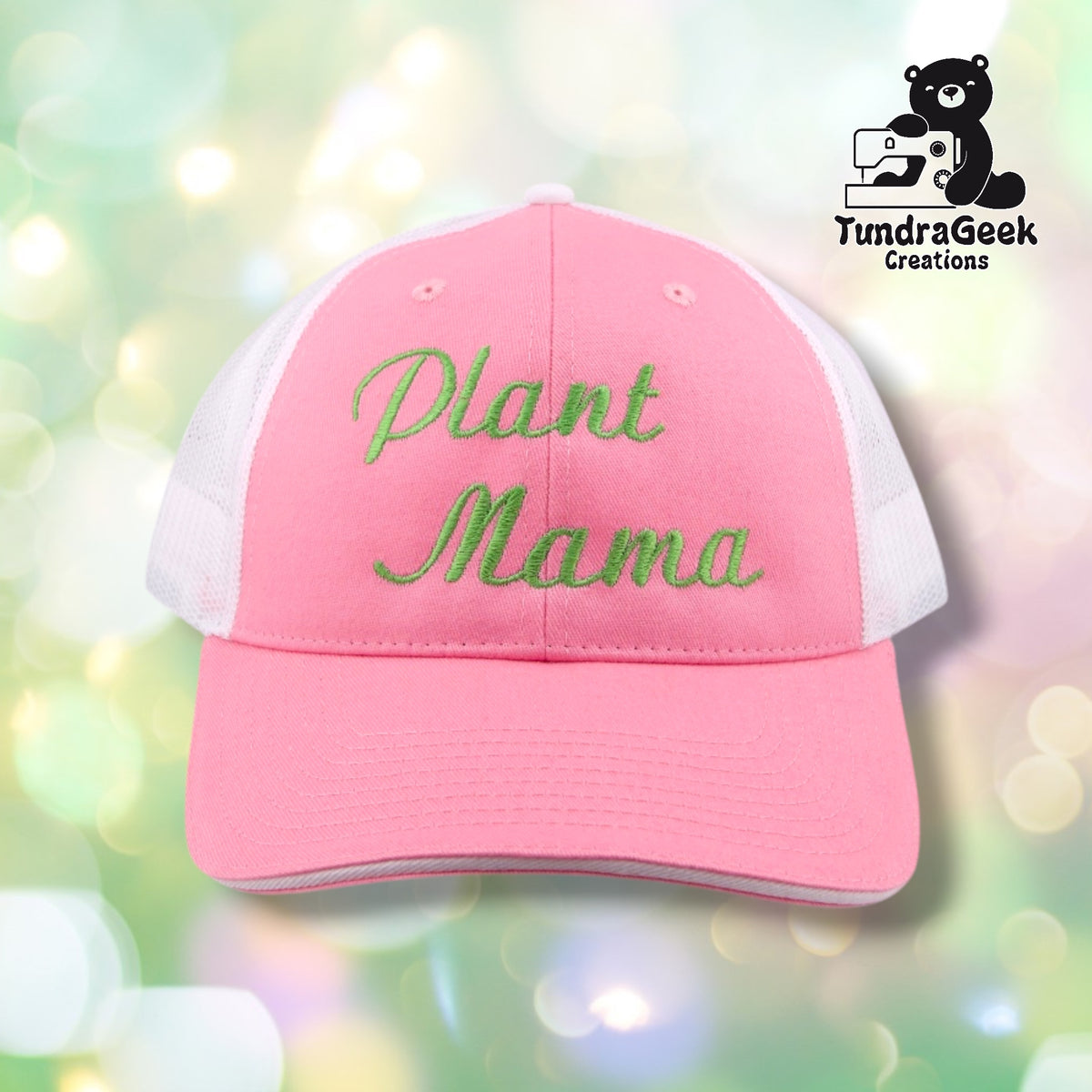 A pink and white trucker cap with green embroidered text reading "Plant Mama" displayed against a soft, blurred green and white bokeh background.