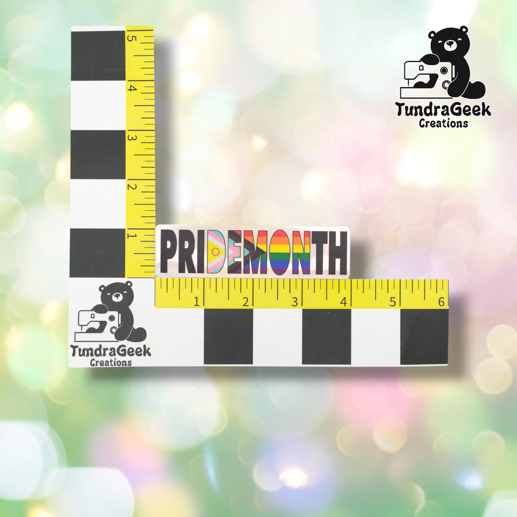 Pride Month sticker positioned against a TundraGeek Creations branded ruler card showing yellow tape measure. Sticker measures approximately 4 inches wide by 1.1 inches tall.