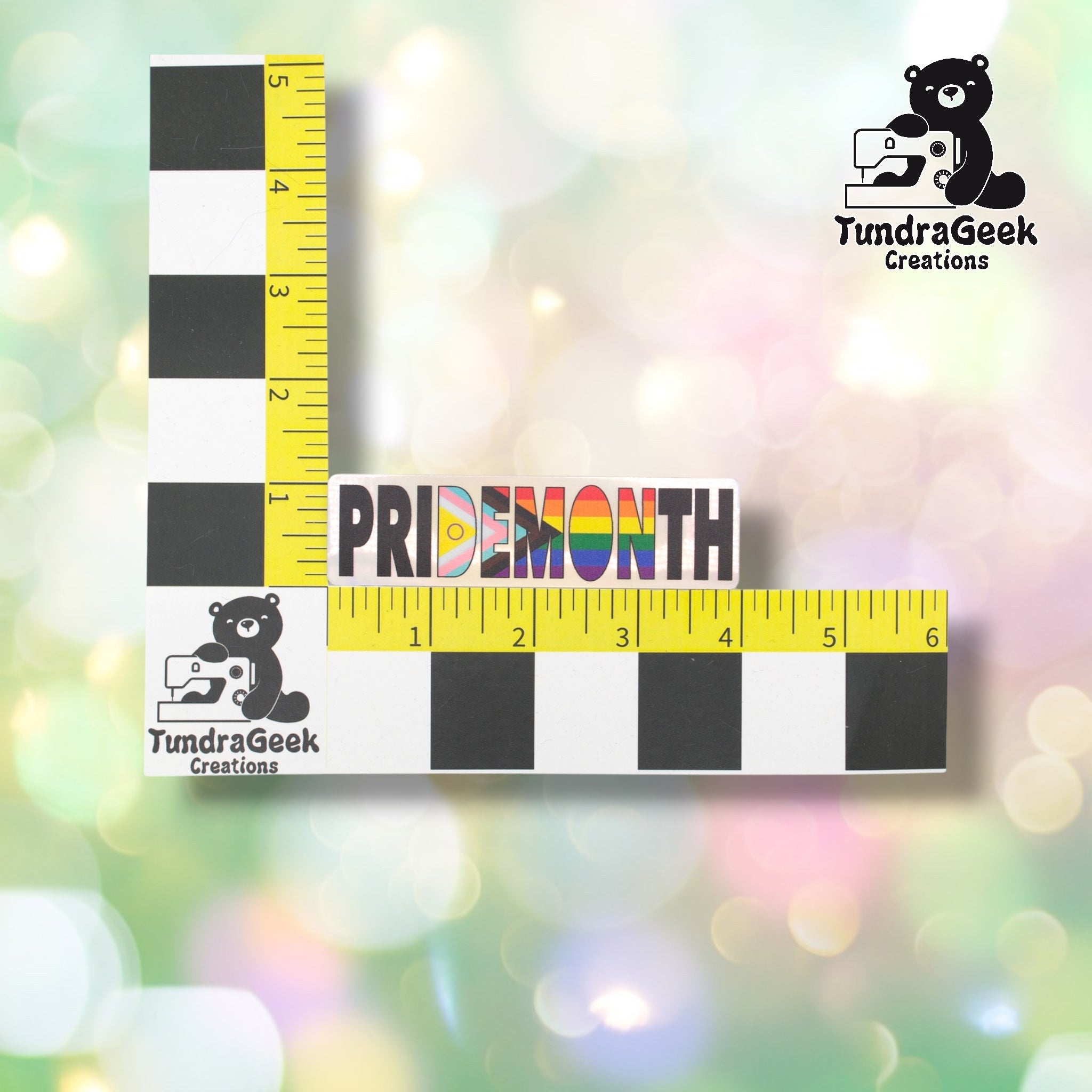 Pride Month sticker positioned against a TundraGeek Creations branded ruler card showing yellow tape measure. Sticker measures approximately 4 inches wide by 1.1 inches tall.