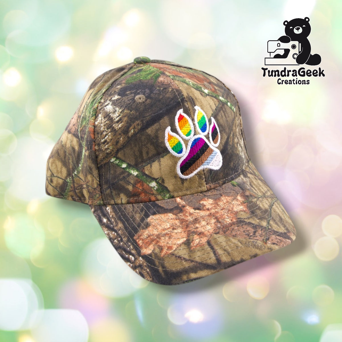 A camouflage baseball cap with a rainbow paw print embroidery patch on the front, displayed against a soft bokeh background.