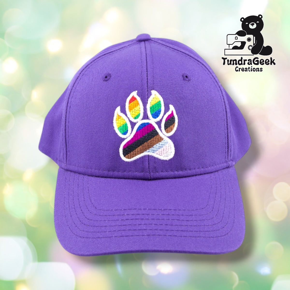 A purple baseball cap with an embroidered rainbow paw print design featuring white outline and multicolored toe beans on a soft-focus bokeh background.