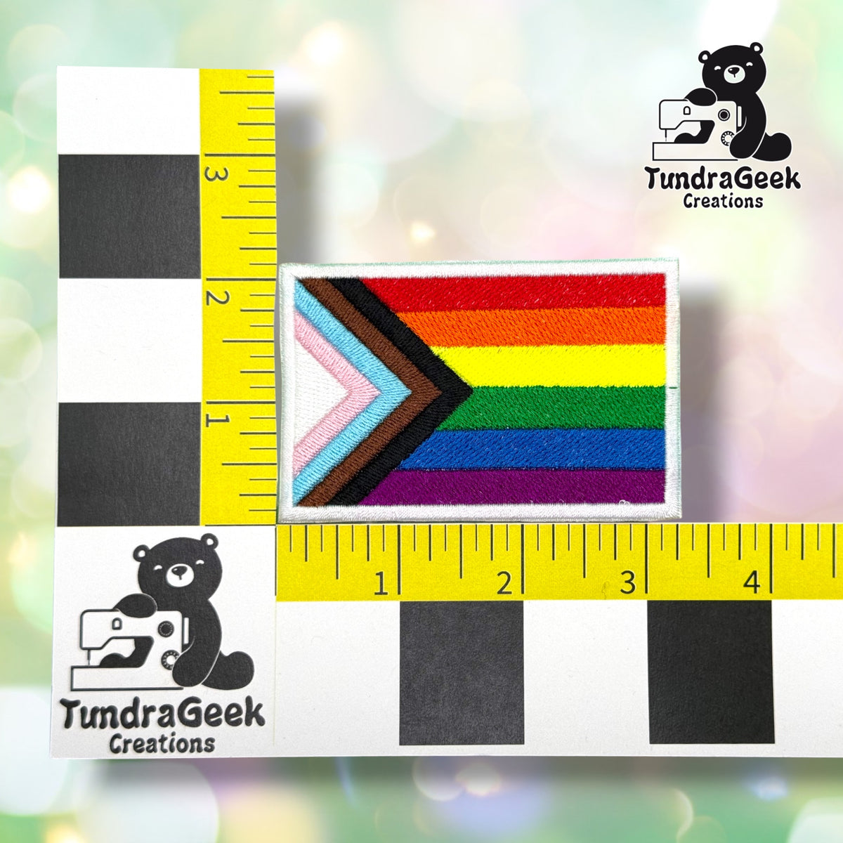 Patch shown against a black-and-white checkered background with a yellow ruler for scale, measuring approximately 3.25 inches wide by 2.25 inches tall.