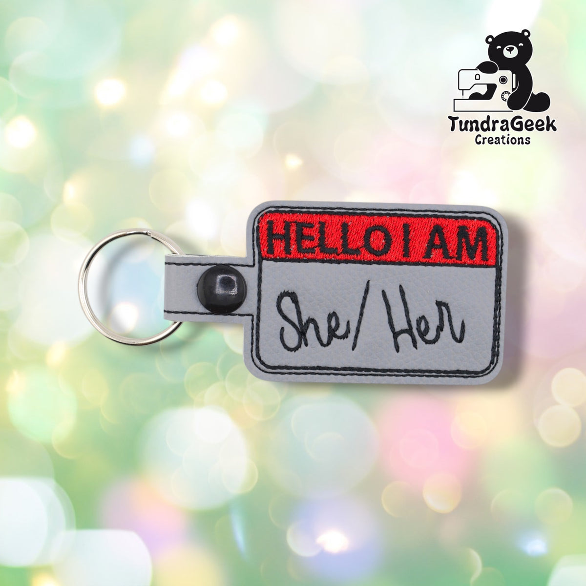 Front view with "She/Her" embroidered in black beneath the red "HELLO I AM" header.