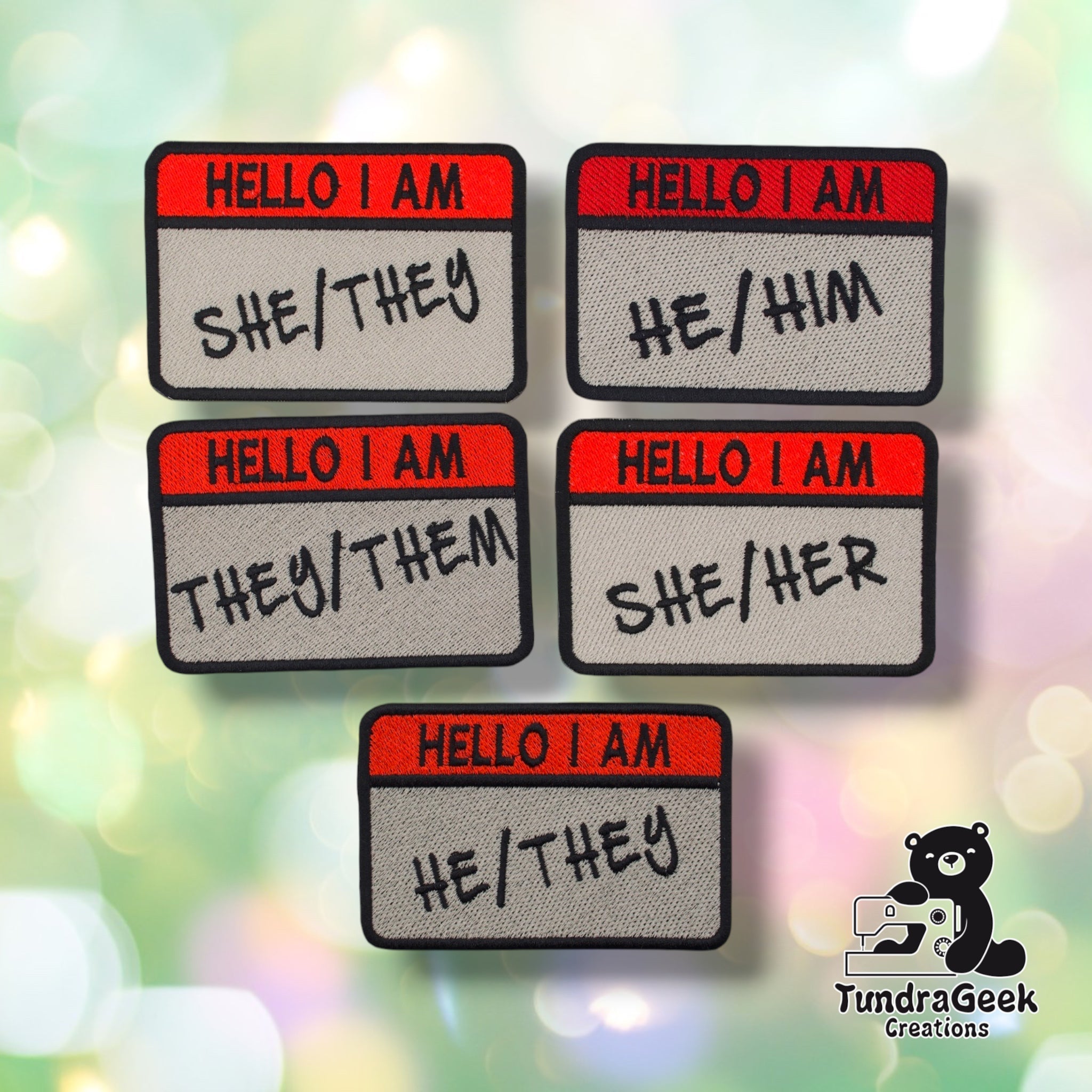 Five nametag-style sew-on patches grouped together, each reading "HELLO I AM" in red with a different pronoun set embroidered below in black — She/They, He/Him, They/Them, She/Her, and He/They.