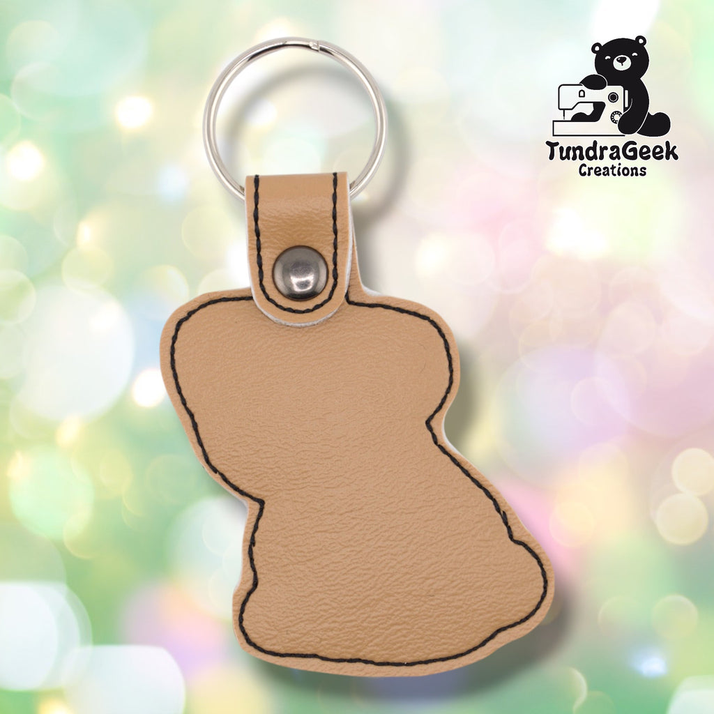 Plain back of the pug keychain showing tan faux leather and black outline stitching following the pug silhouette. Silver metal rivet closure at top. No embroidery on reverse.