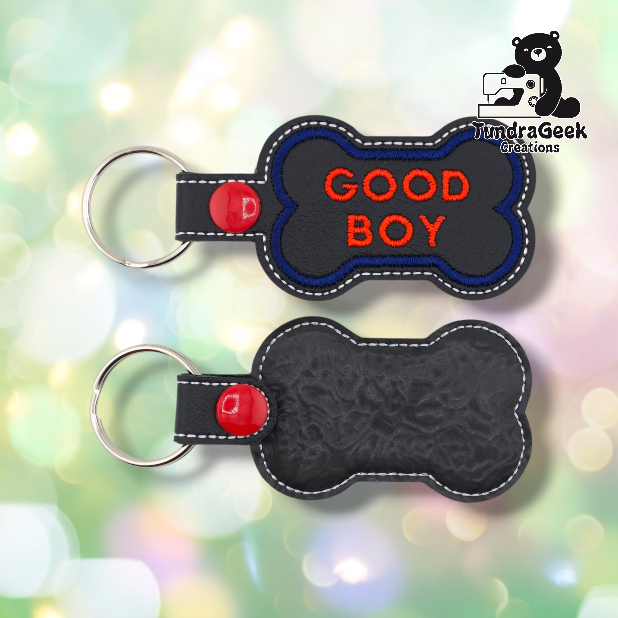 Two views of the “GOOD BOY” keychain. Front: black vinyl with blue border and red “GOOD BOY” text in two lines, white edge stitching, red snap and split ring. Back: black textured vinyl with white edge stitching and red snap hardware.