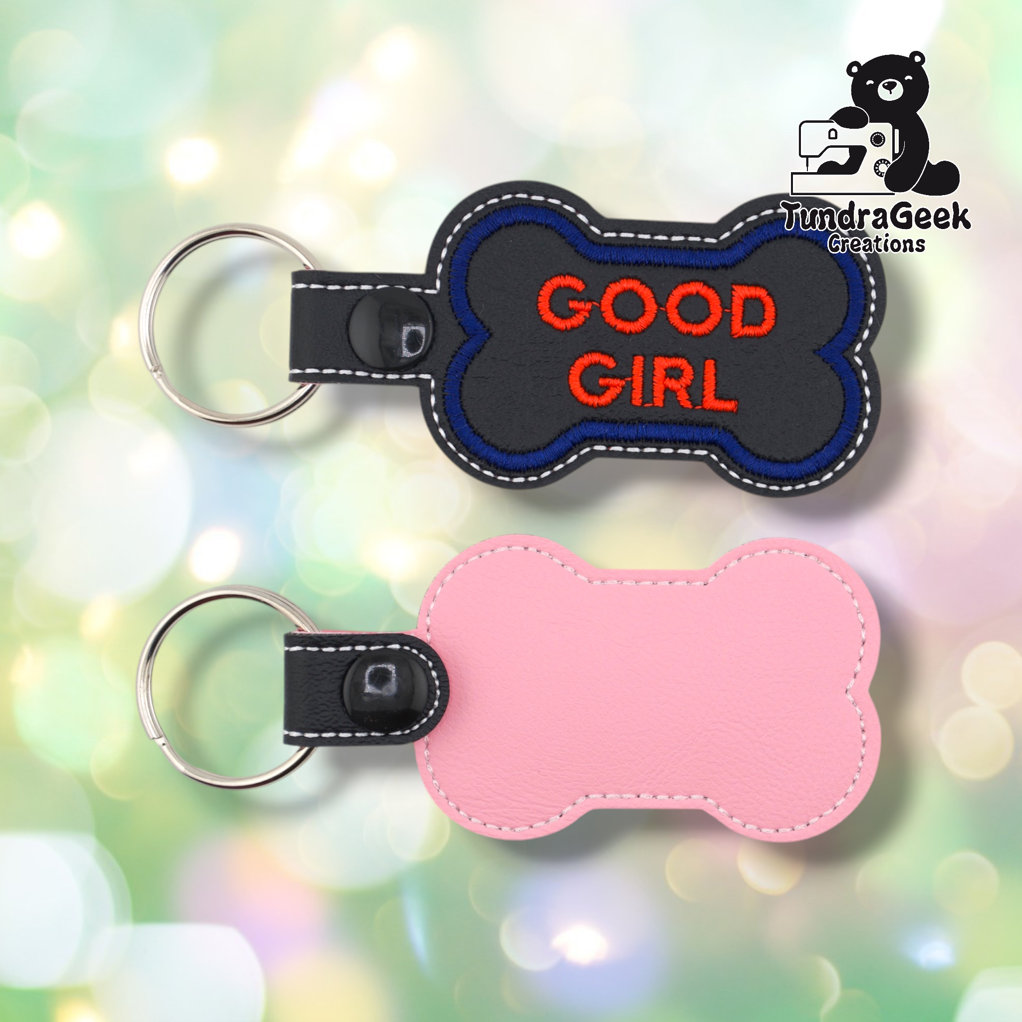 Two views of the “GOOD GIRL” keychain. Front: black vinyl with blue border and red “GOOD GIRL” text in two lines, white edge stitching, black snap and split ring. Back: pink vinyl with white edge stitching and black snap hardware