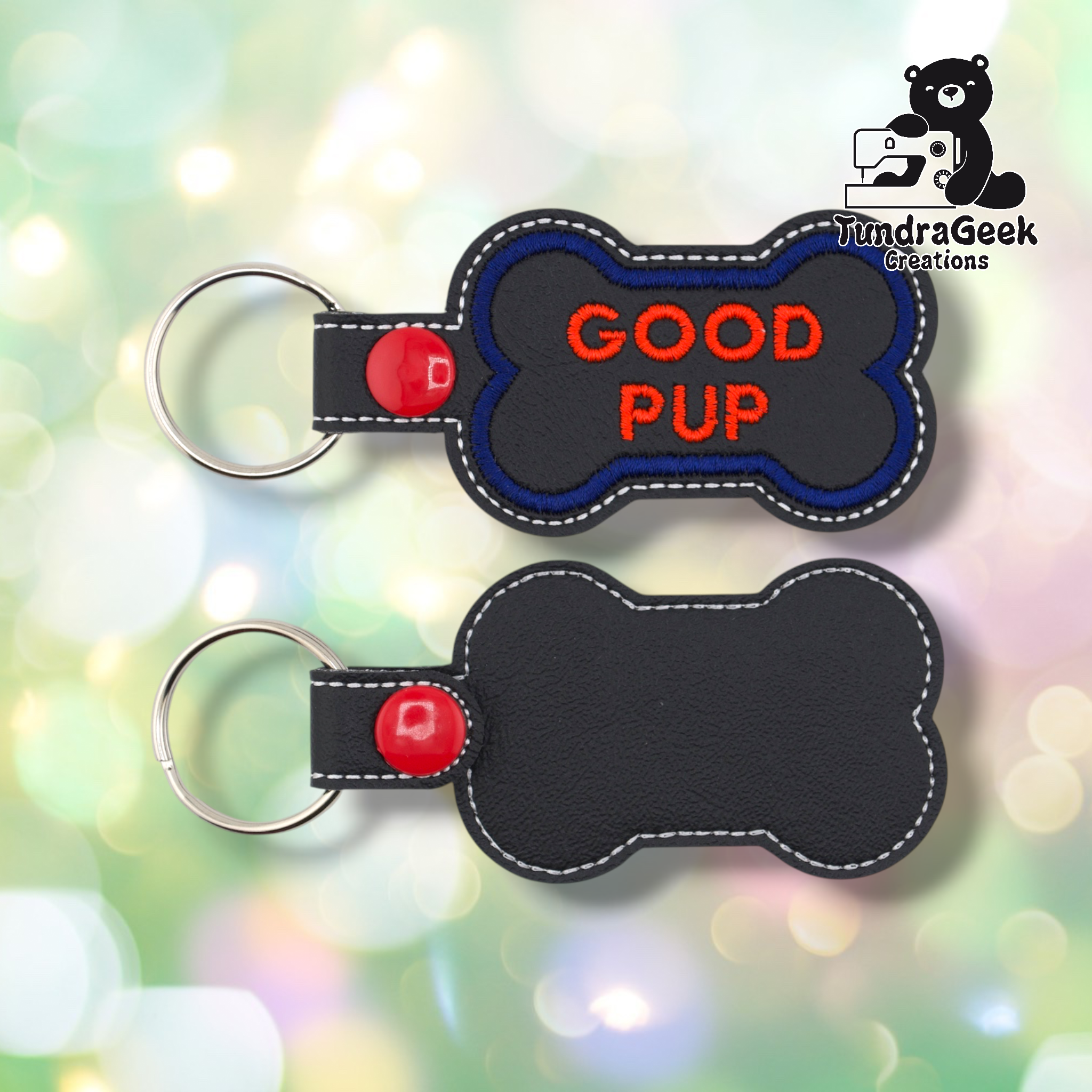 Two views of the “GOOD PUP” keychain. Front: black vinyl with blue border and red “GOOD PUP” text in two lines, white edge stitching, red snap and split ring. Back: plain black vinyl with white edge stitching and red snap hardware