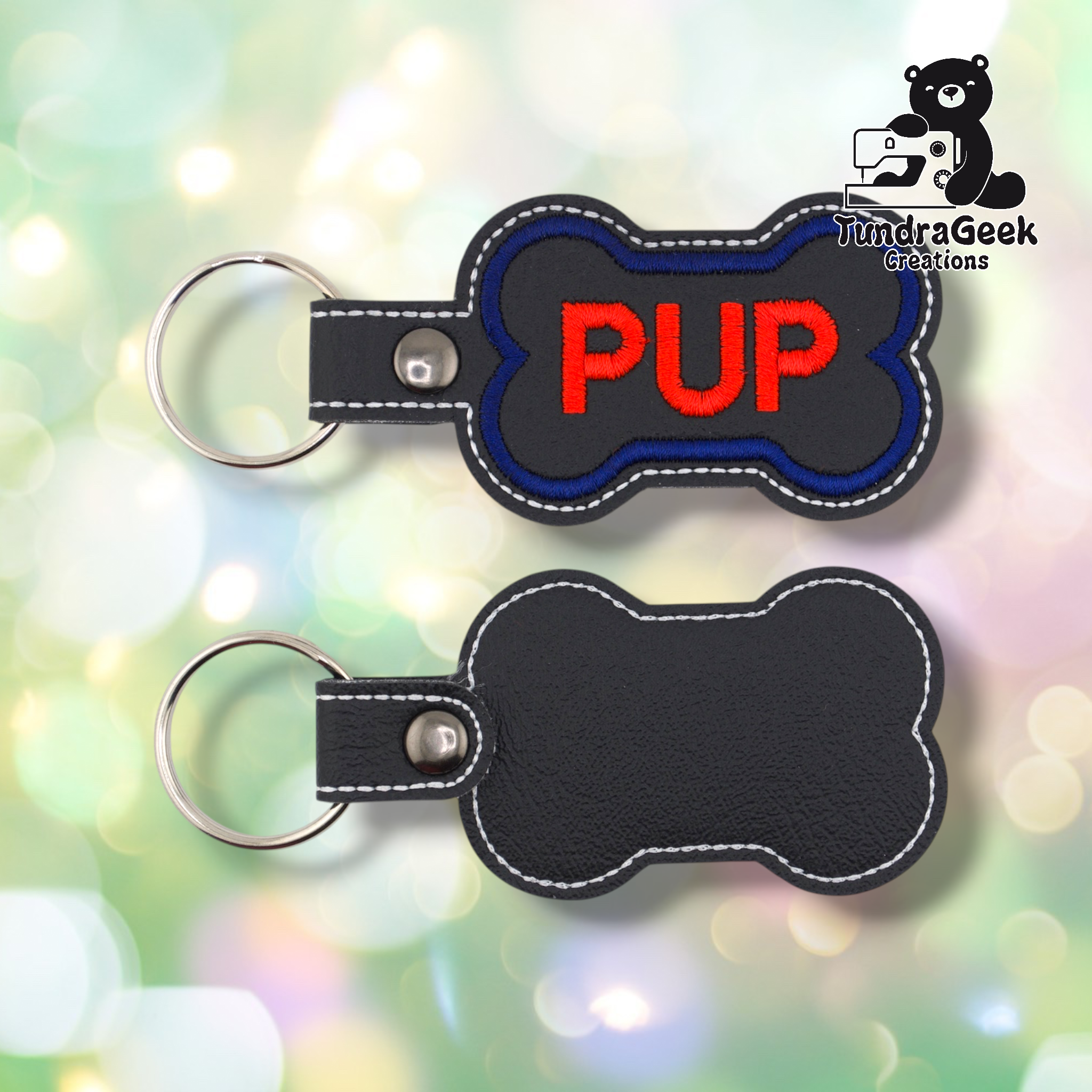 Two views of the “PUP” keychain showing front and back. Front: black vinyl with blue border and red “PUP” text, white edge stitching, silver snap and split ring. Back: plain black vinyl with white edge stitching and silver snap hardware.
