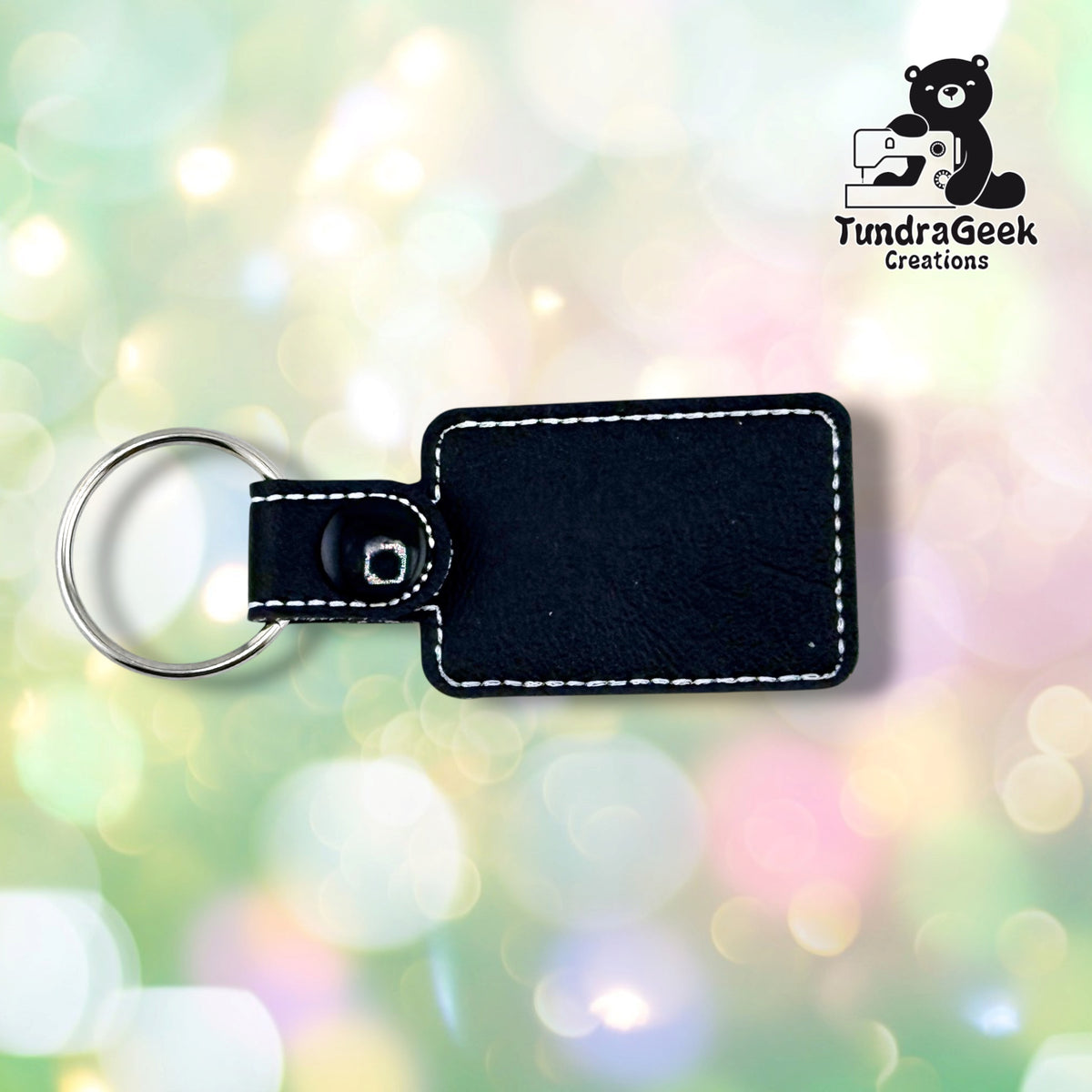The back of the keychain, plain black vinyl with white topstitching following the edge. The black plastic snap and silver split ring are at the left.