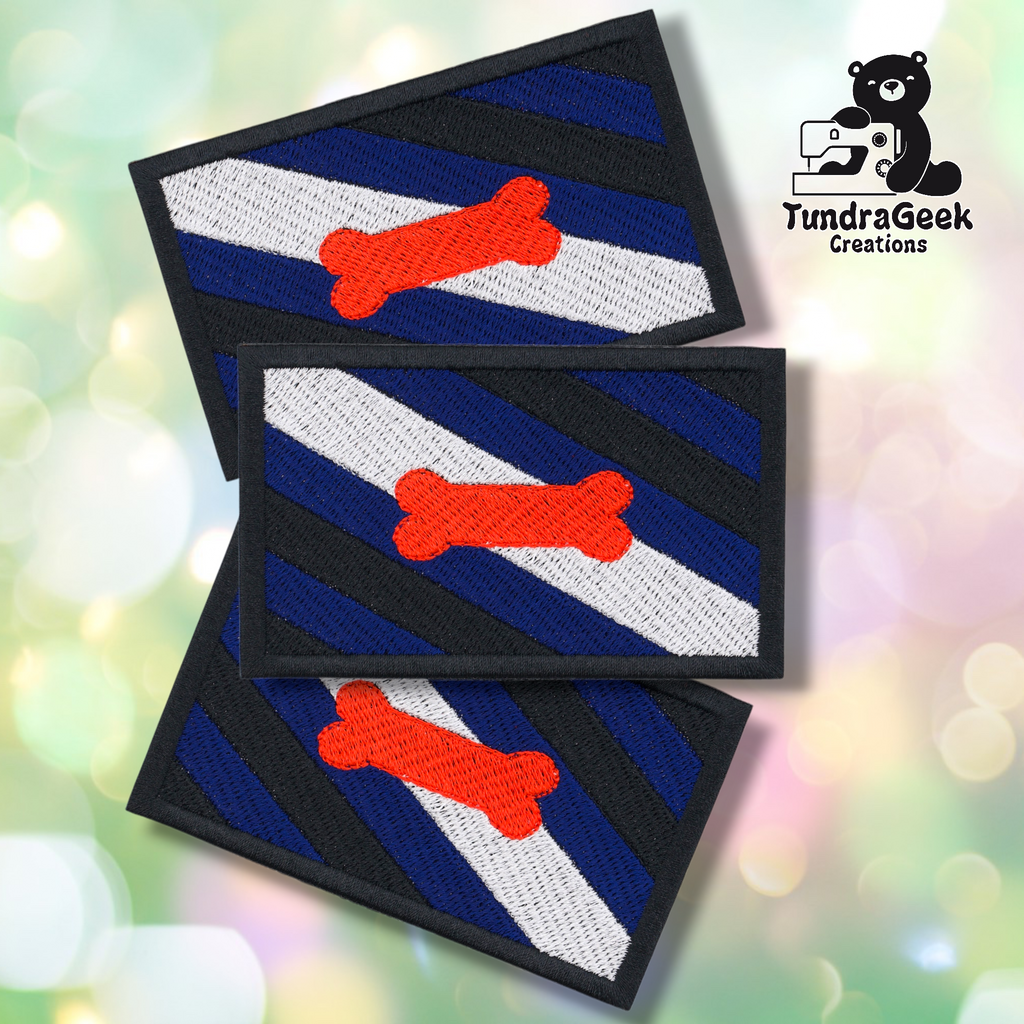 Three rectangular Pup Pride Flag Patches with blue, black, white, and gray diagonal stripes and a red bone in the center overlap. The TundraGeek Creations logo is in the top right. Embroidered sew-on patch with iron-on backing.