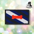 The Pup Pride Flag Patch features diagonal black, blue, and white stripes with an orange bone in the center, plus a TundraGeek Creations cartoon bear logo in the top right. Perfect embroidered sew-on patch for pup play gear with iron-on backing.