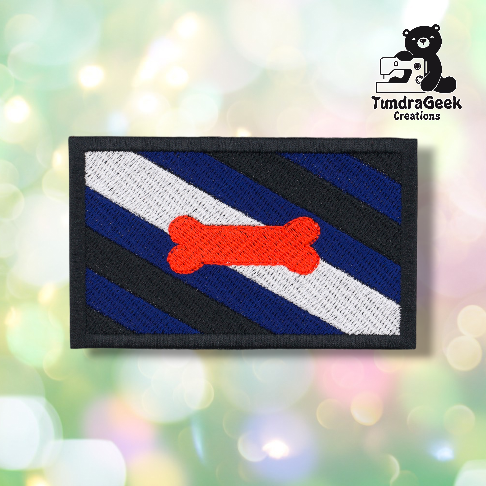 The Pup Pride Flag Patch features diagonal black, blue, and white stripes with an orange bone in the center, plus a TundraGeek Creations cartoon bear logo in the top right. Perfect embroidered sew-on patch for pup play gear with iron-on backing.