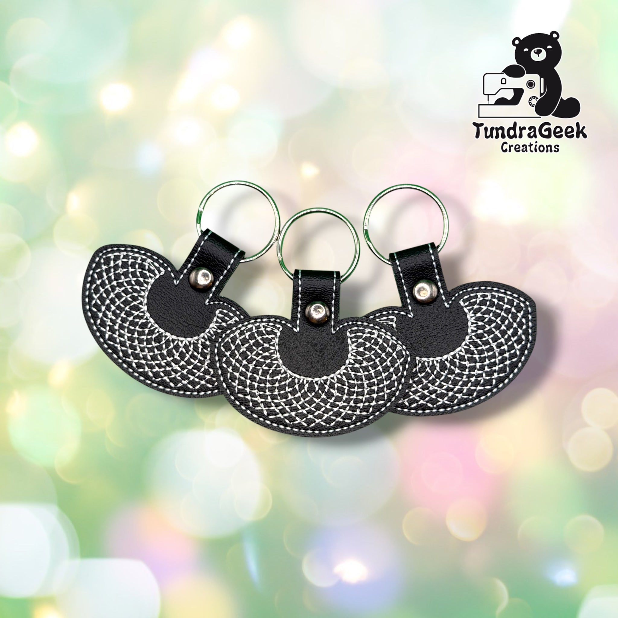 Three identical RBG collar keychains fanned out together, each on a green metal split ring, showing the same black vinyl body and white collar embroidery.