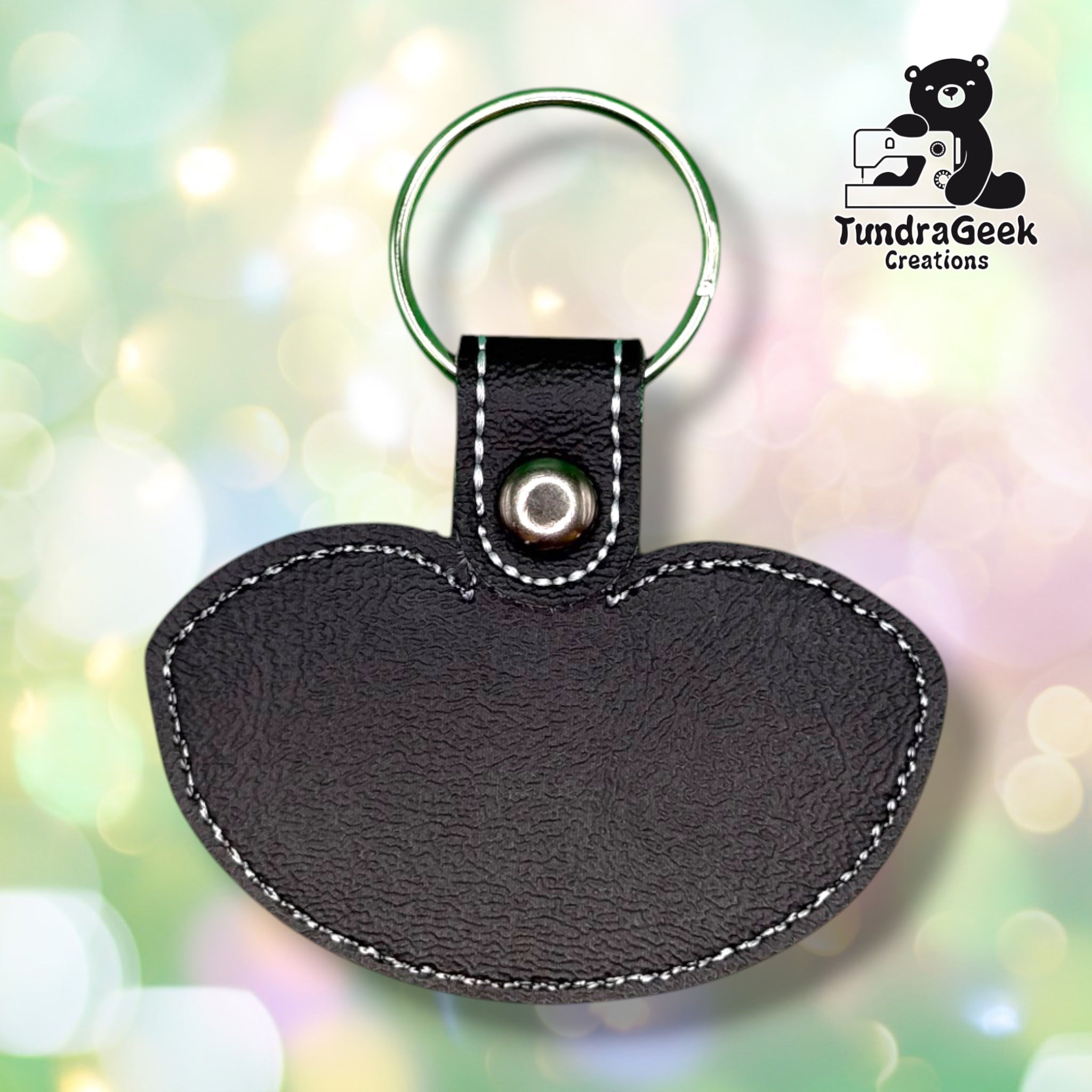 Back of the keychain, showing a plain black vinyl reverse side with white outline stitching following the collar silhouette. Green metal split ring and silver snap closure at top.