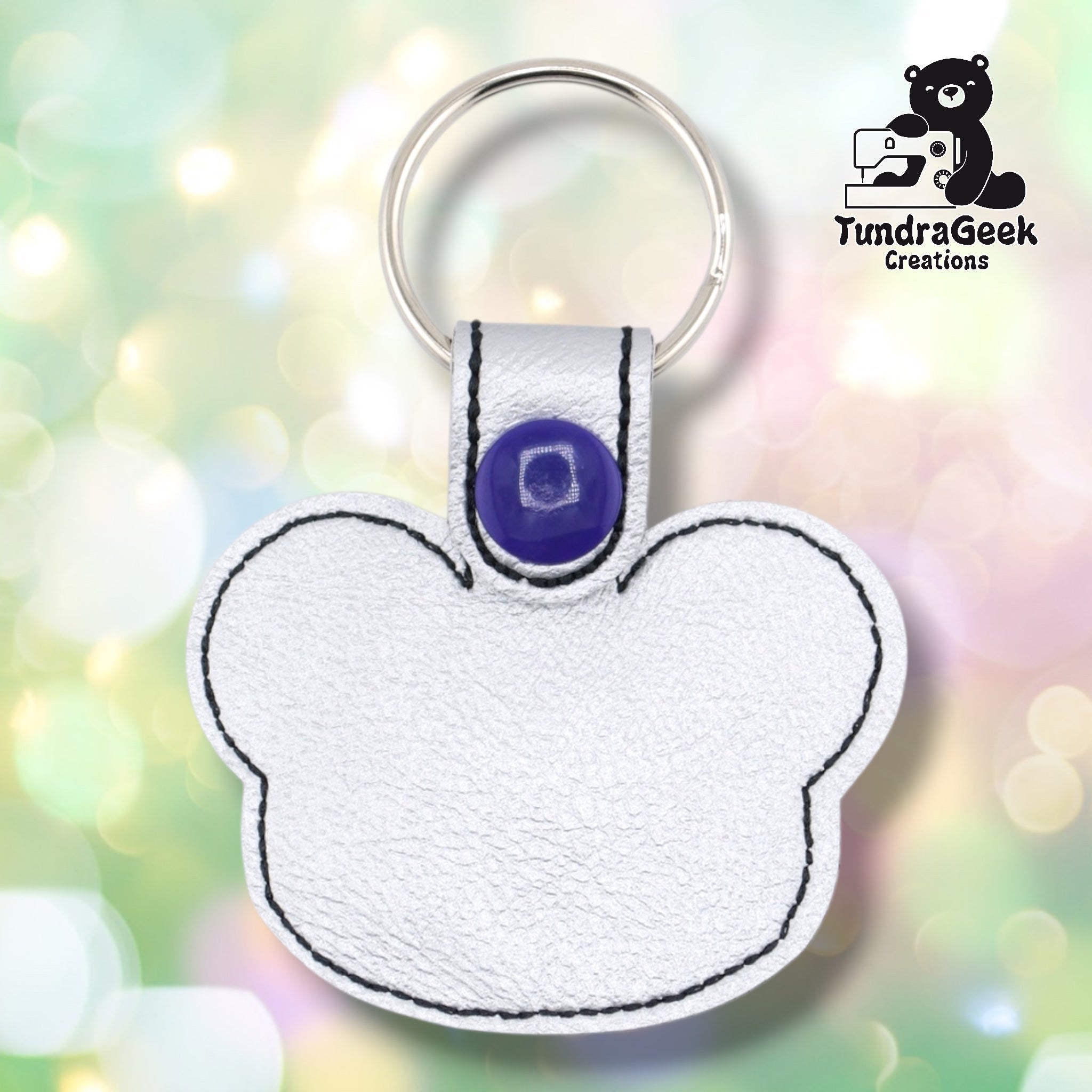 Plain back of the silver metallic panda keychain showing pearlescent faux leather, black outline stitching following the panda head shape, and purple snap closure. No embroidery on reverse.