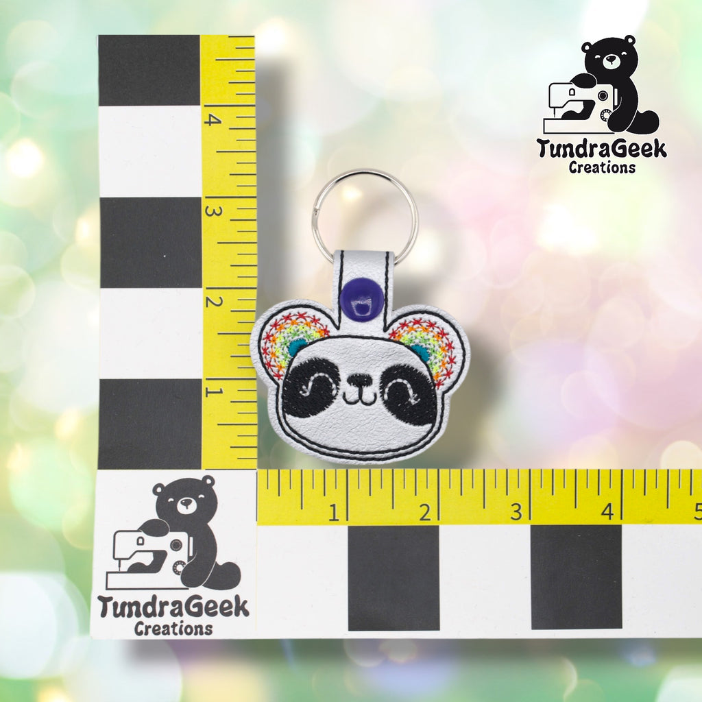 Silver panda keychain positioned against a TundraGeek Creations branded ruler card showing yellow tape measure. Keychain body measures approximately 2.5 inches wide by 1.75 inches tall, not including hardware.