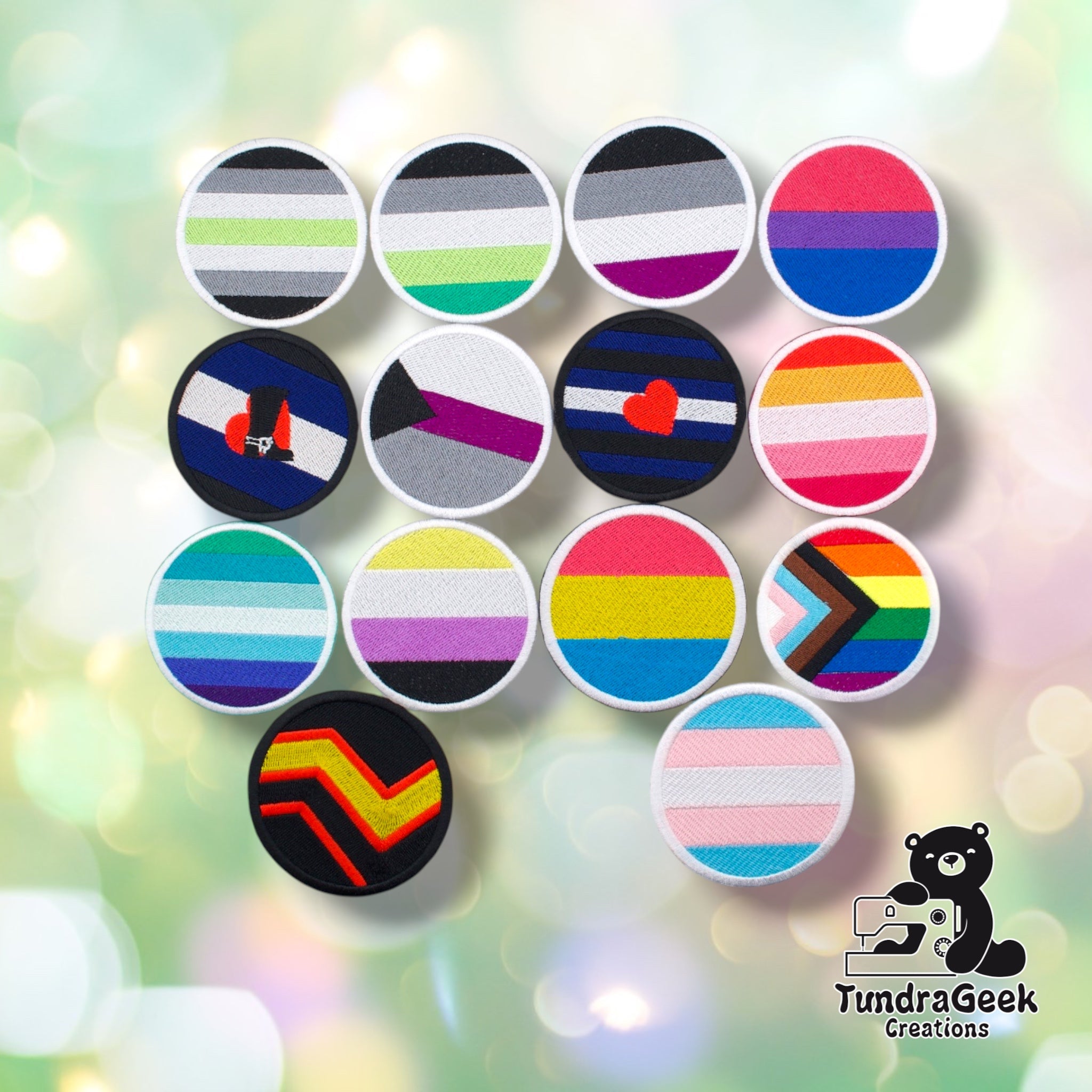 Thirteen embroidered pride flag patches in various colors arranged in a circle on a pastel gradient background, with TundraGeek Creations logo in the top right.