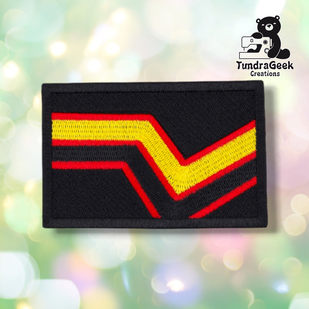 Black rectangular patch with full-coverage embroidery, showing a yellow chevron outlined in red running diagonally from the lower left to the upper right, in the pattern of the rubber and latex pride flag.