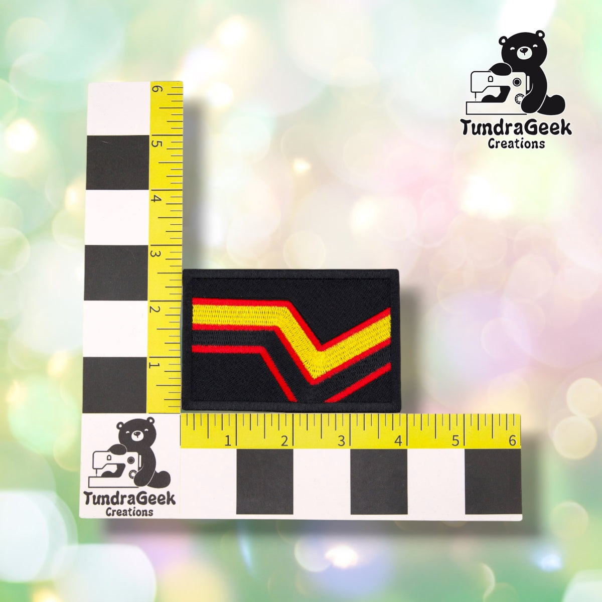 The patch photographed against a yellow ruler marked in inches along both edges, for size reference. It measures 4 inches wide by 2.5 inches tall.  ---