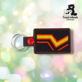 Black rectangular vinyl keychain embroidered with a yellow chevron outlined in red running from the lower left to the upper right, matching the rubber and latex pride flag. Orange topstitching follows the edge, and a red plastic snap closes the tab around a silver split ring.