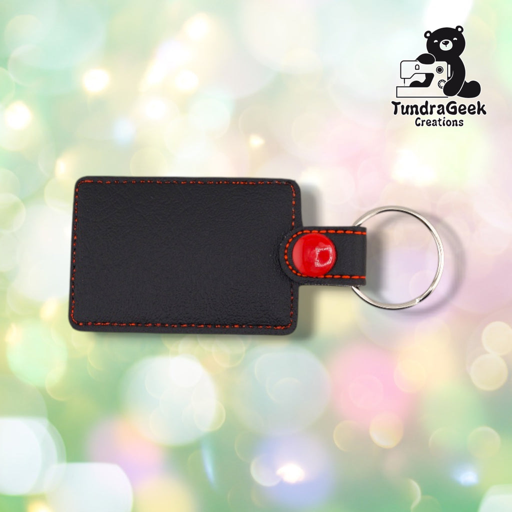 The back of the keychain, plain black vinyl with orange topstitching following the edge. The red plastic snap and silver split ring are visible at the top.