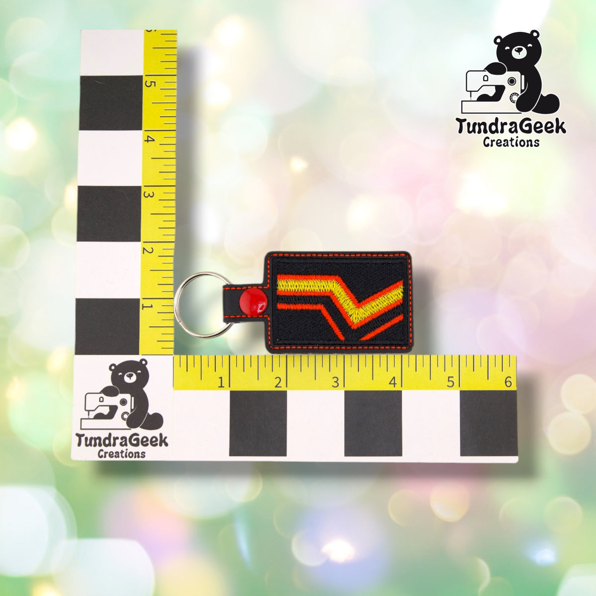 The keychain photographed against a yellow ruler marked in inches along both edges, for size reference. It measures 4.25 inches long by 2 inches tall.  ---