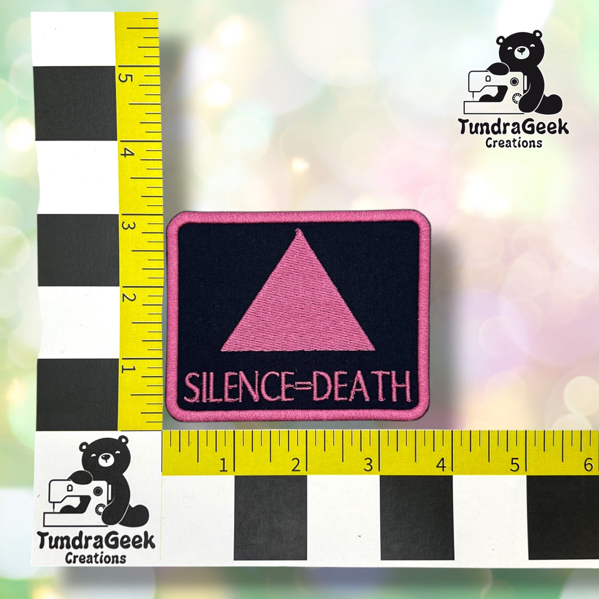 Rectangular variant shown against a black-and-white checkered background with yellow rulers for scale, measuring approximately 3.75 inches wide by 3 inches tall.