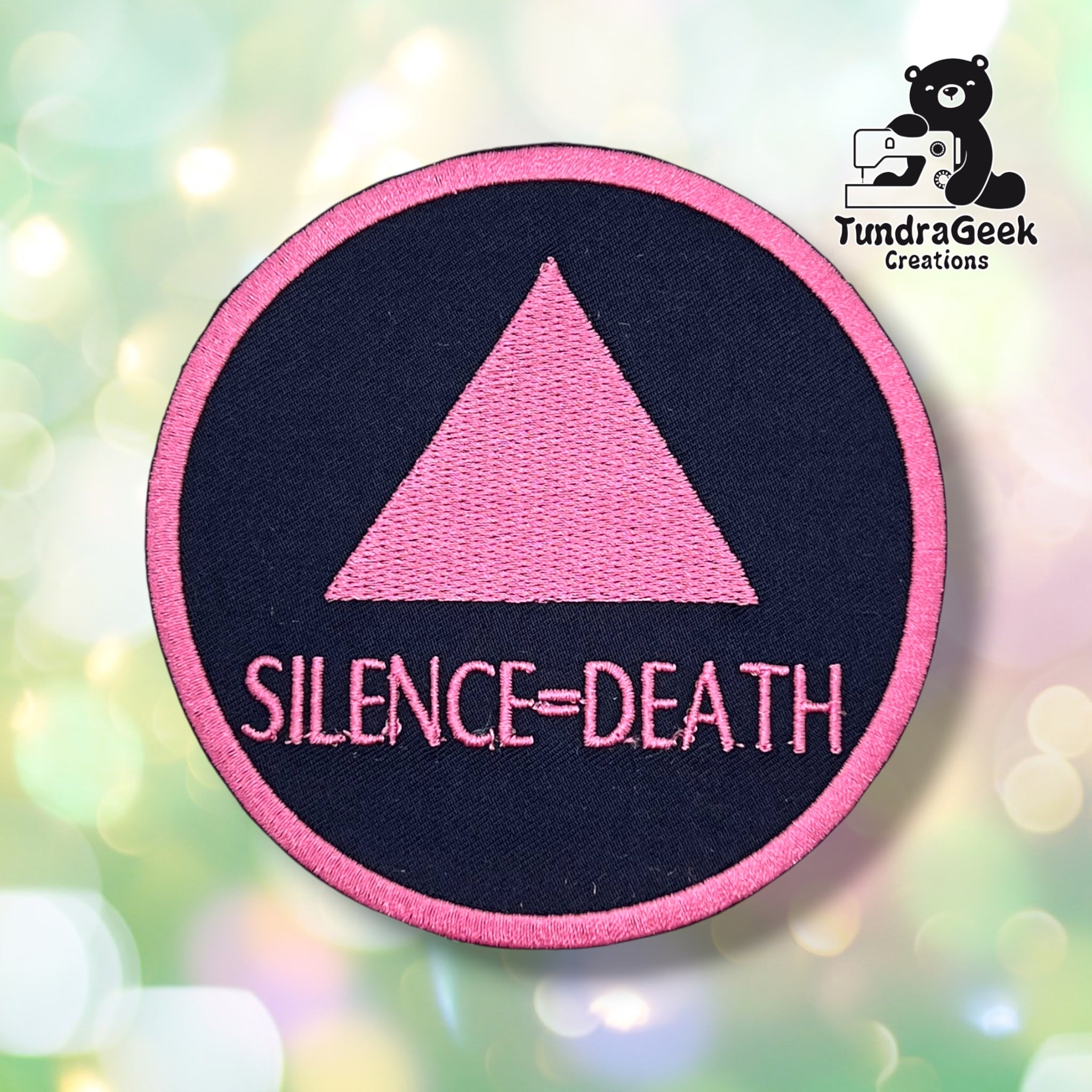 Front view of the round variant: a black circular patch with a pink merrowed edge, embroidered with a solid pink triangle above "SILENCE=DEATH" in pink block lettering.