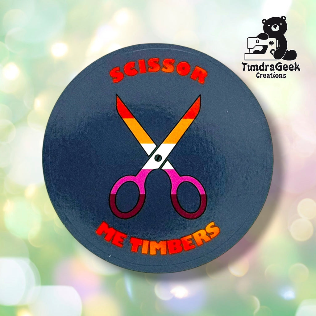 Close-up of the Lavender colorway, showing crossed scissors in lesbian pride gradient colors and "Scissor Me Timbers" text arced around them. Background color in this shot leans navy-gray due to lighting/camera limitations rather than true lavender.