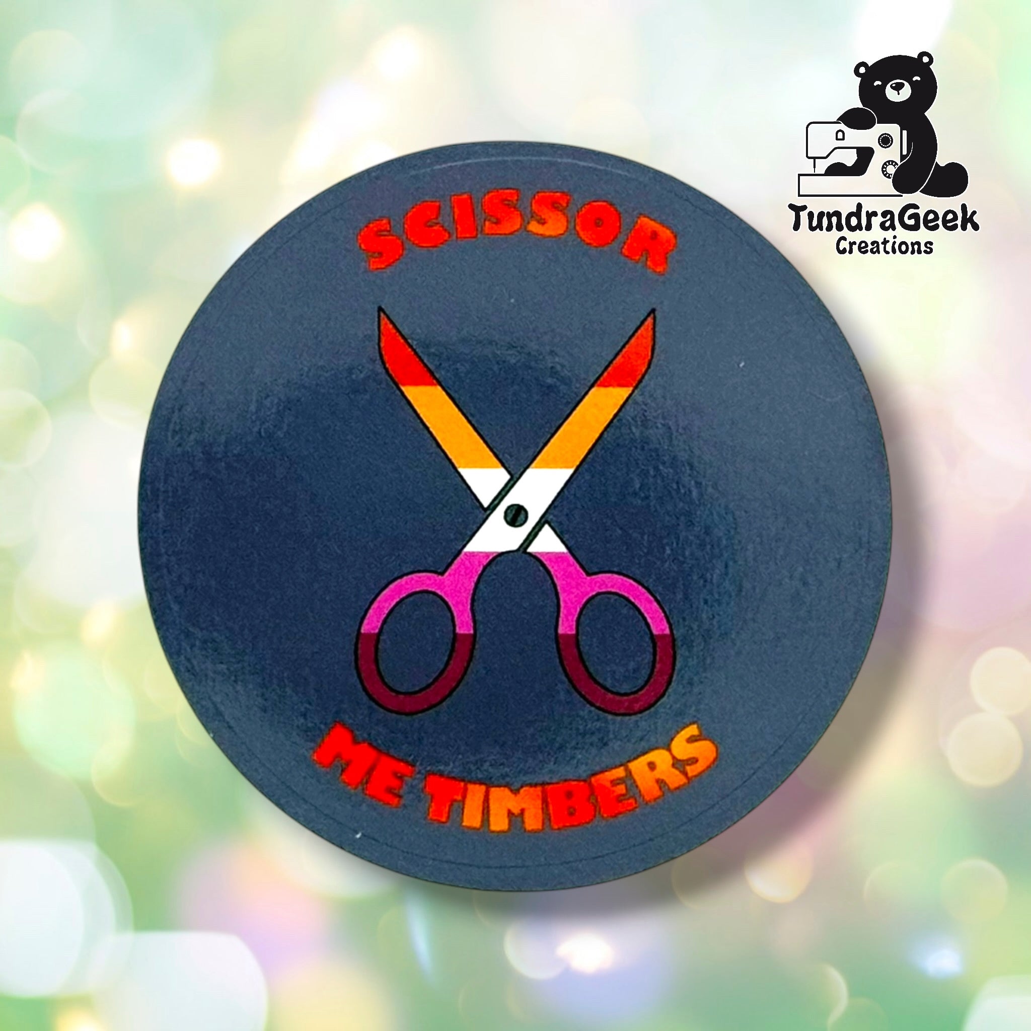 Close-up of the Lavender colorway, showing crossed scissors in lesbian pride gradient colors and "Scissor Me Timbers" text arced around them. Background color in this shot leans navy-gray due to lighting/camera limitations rather than true lavender.