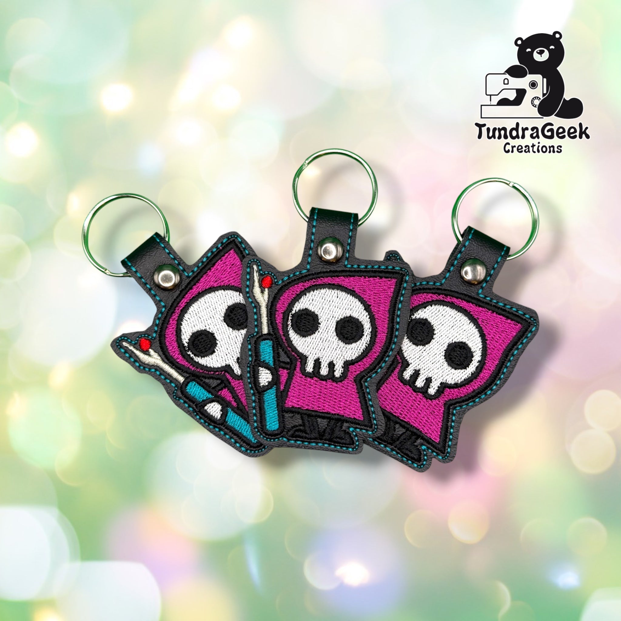 Three identical Seam Reaper keychains fanned out together, each on a green metal split ring, showing the same hooded skull and seam ripper design.