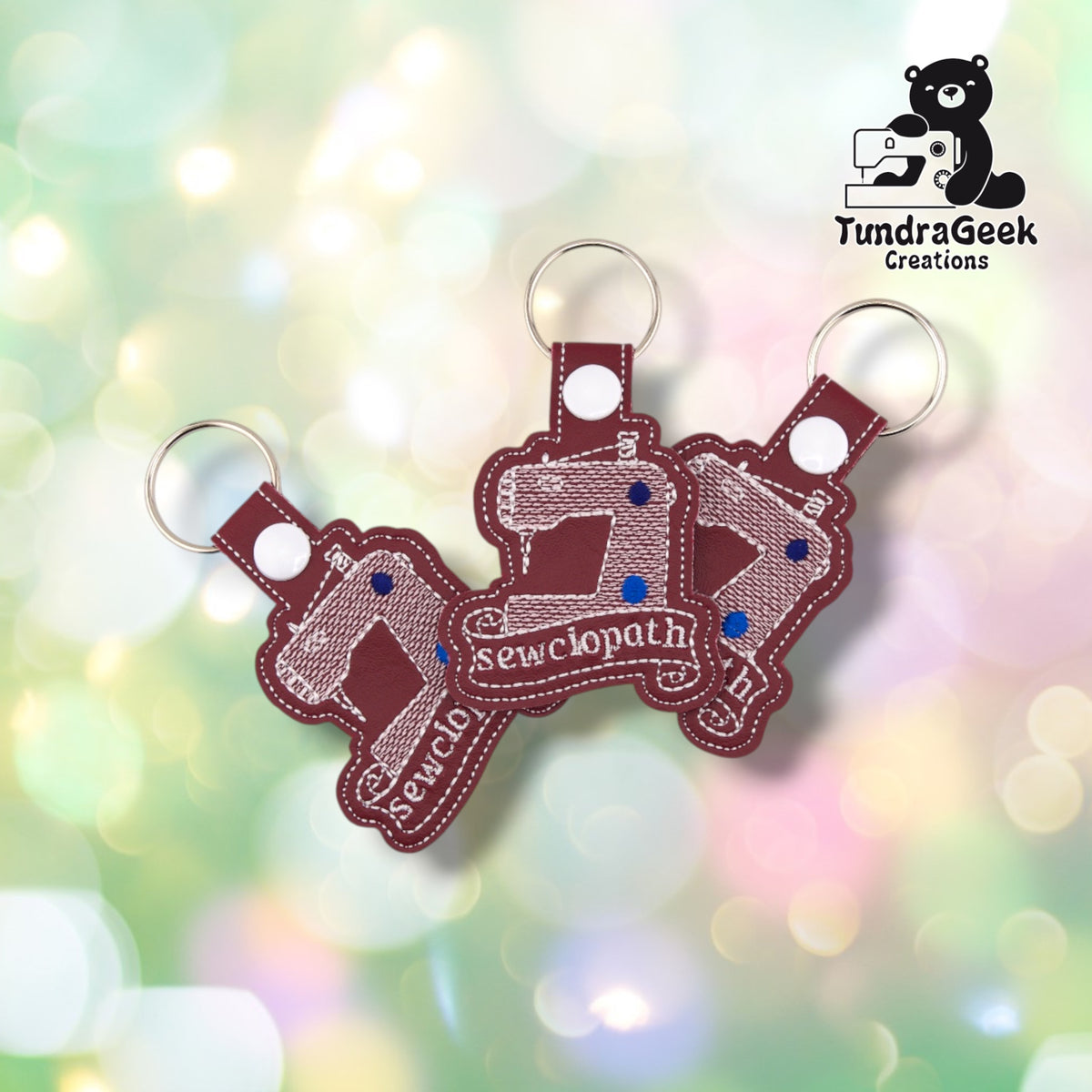Three identical Sewciopath keychains fanned out at different angles, each in maroon faux leather with the same white sewing machine design and script banner.
