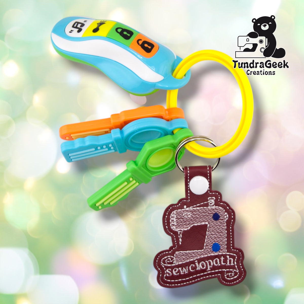 The keychain clipped to a yellow silicone bangle keyring alongside a set of colorful plastic toy keys, showing it in everyday use.