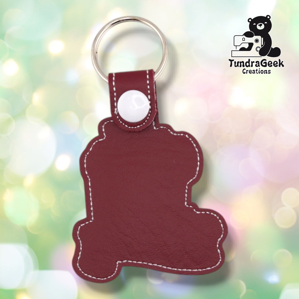 The back of the keychain, plain maroon faux leather with white topstitching following the outline. The white plastic snap and silver split ring are at the top.