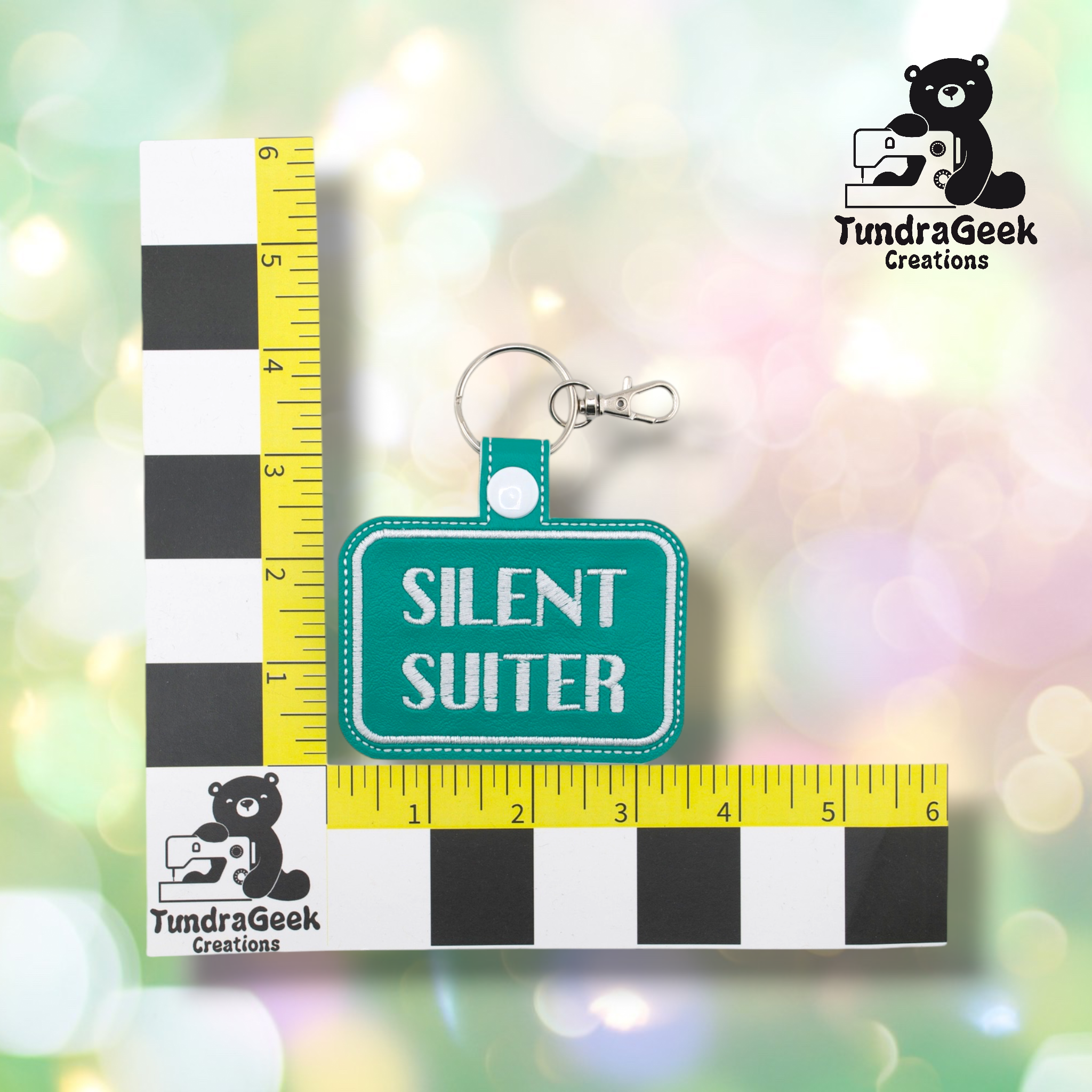 A teal keychain reading SILENT SUITER is displayed against a colorful background with a size scale and the TundraGeek Creations logo.