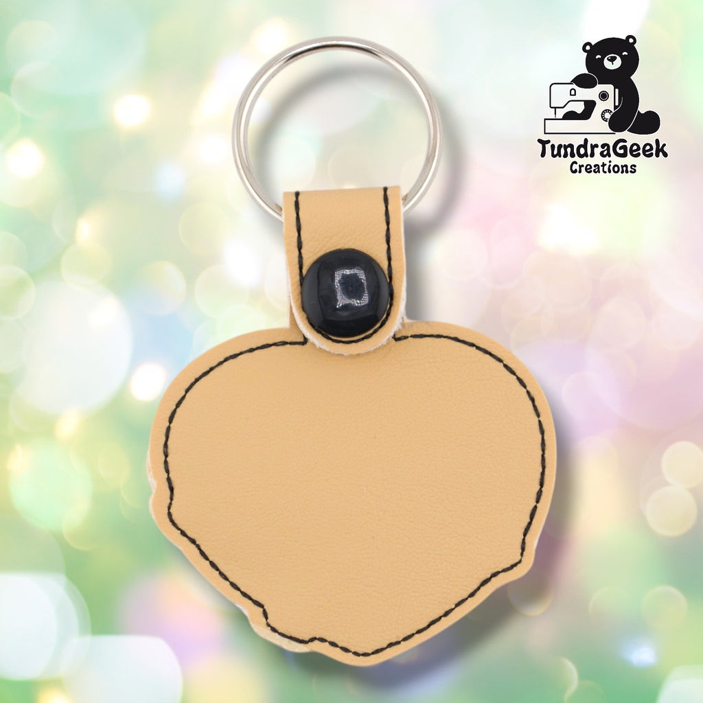 Plain back of the sloth heart keychain showing tan faux leather and black outline stitching following the heart shape. Black snap closure at top. No embroidery on reverse.