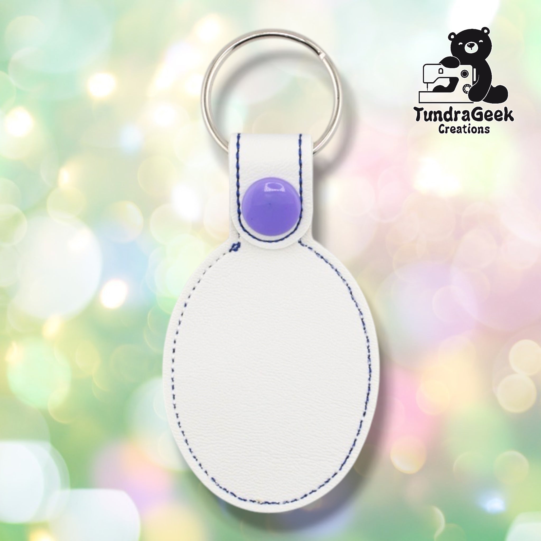 Plain back of the spooky flowers keychain showing white faux leather and navy outline stitching following the oval shape. Purple plastic snap closure at top. No embroidery on reverse.