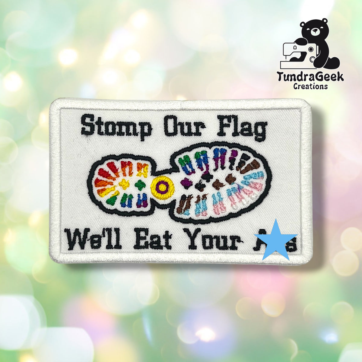 Front view of the patch with a blue star covering part of the bottom text, for use on platforms or in contexts where the uncensored text isn't appropriate. The visible text reads "Stomp Our Flag" above a boot-sole shape in rainbow and trans flag colors, with "We'll Eat Your A[covered]s" below.