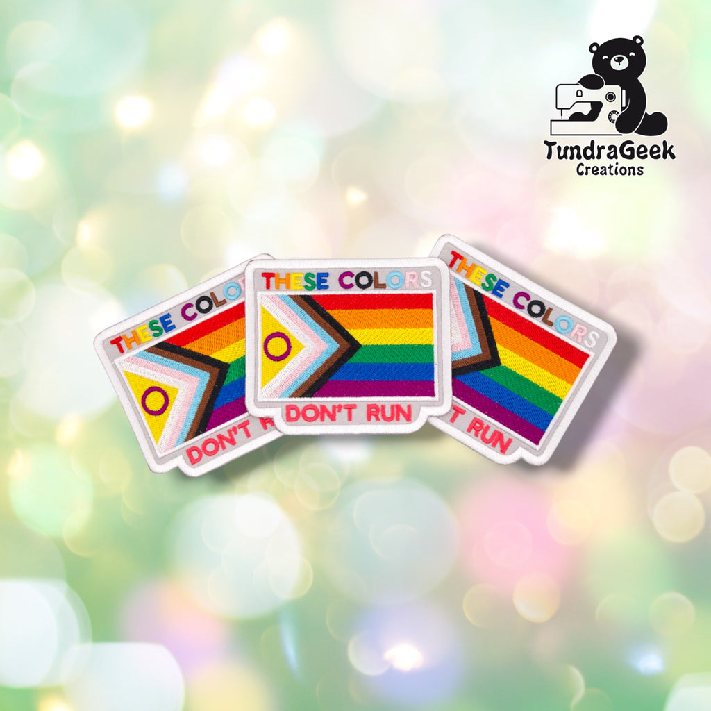 Three identical These Colors Don't Run patches fanned out together, each showing the same rainbow text, Progress Pride flag, and red lettering.