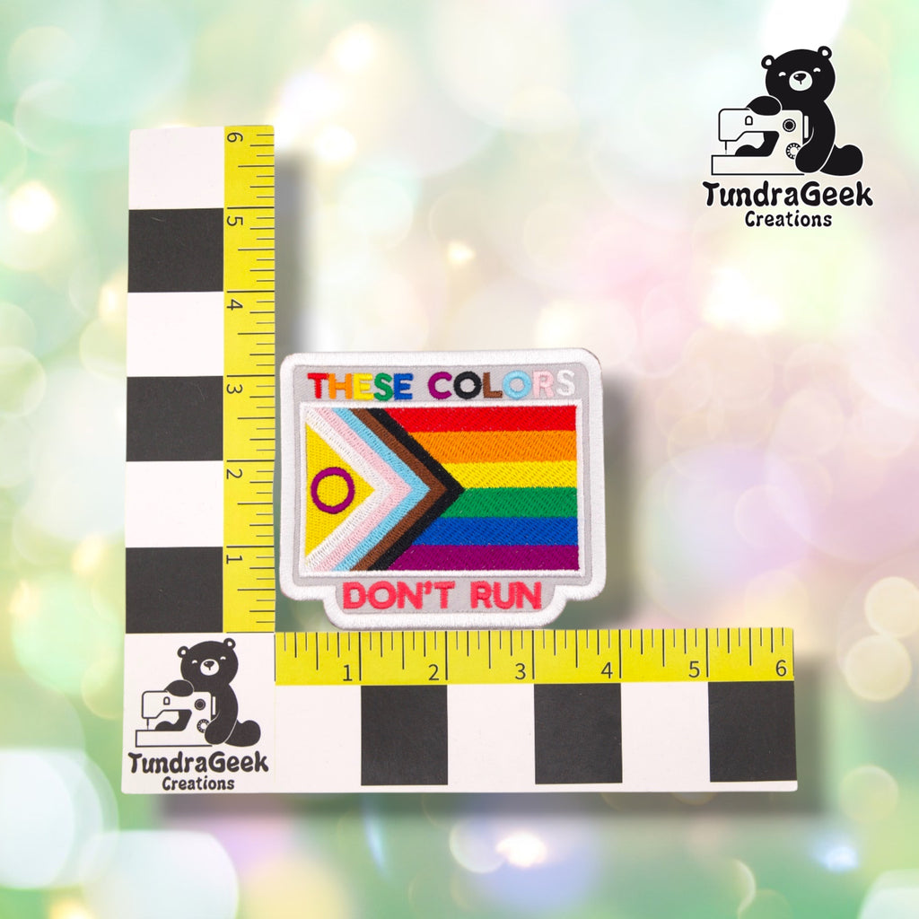 Patch shown against a black-and-white checkered background with a yellow ruler for scale, measuring approximately 4 inches wide by 3.25 inches tall.