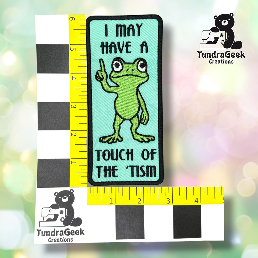 Patch shown against a black-and-white checkered background with yellow rulers for scale, measuring approximately 6 inches tall by 2.75 inches wide.