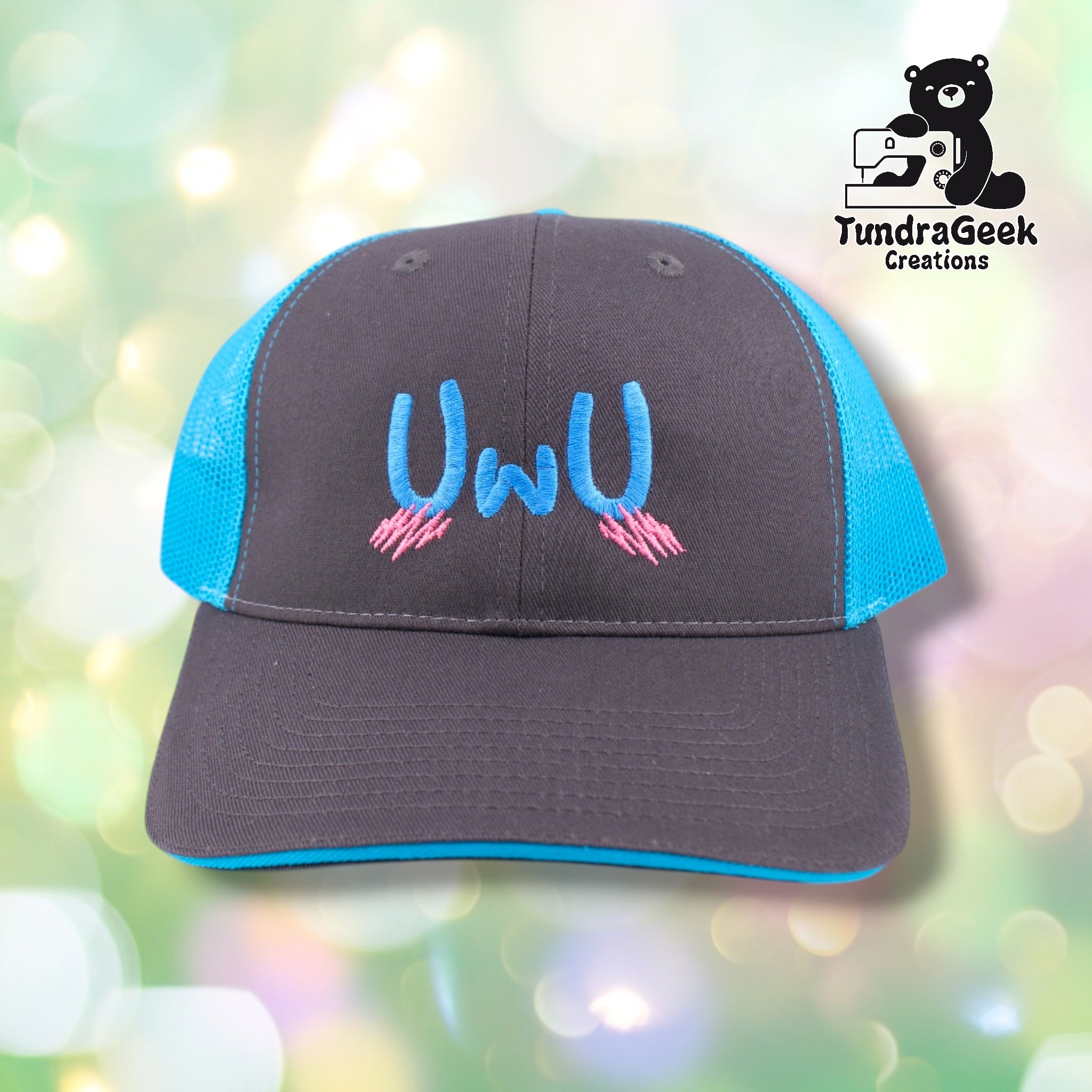 A charcoal and bright blue trucker-style cap with embroidered blue "UwU" text and pink striped details on the front.
