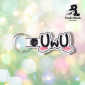 White vinyl keychain embroidered with "UwU" in bold black lettering, with pink blush marks beneath each U. A black plastic snap closes the tab around a silver split ring.