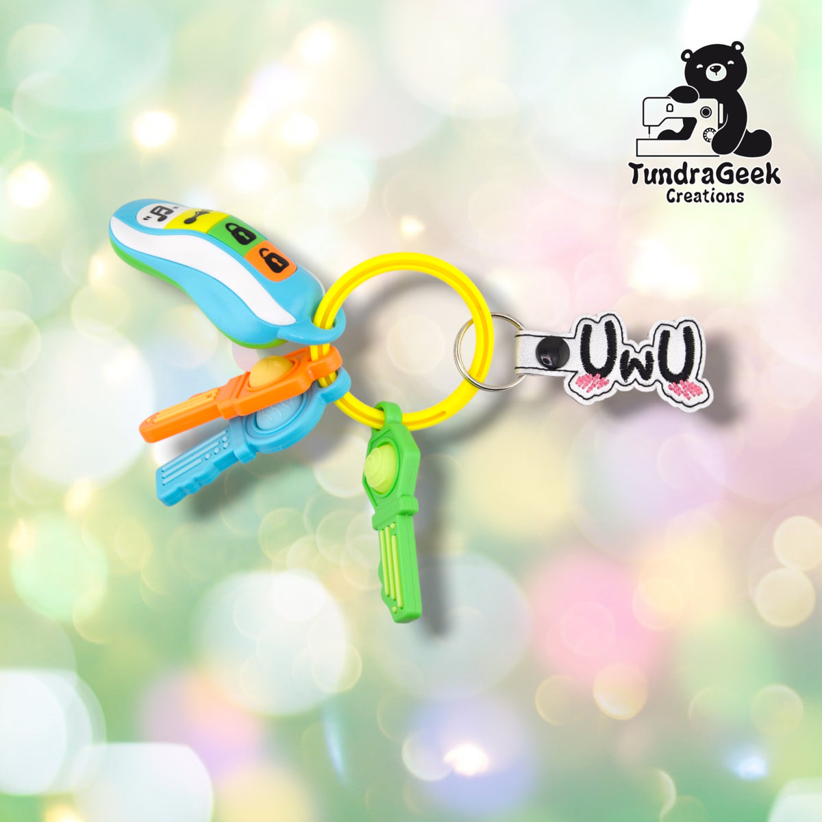 The keychain clipped to a yellow silicone bangle keyring alongside a set of colorful plastic toy keys, showing it in everyday use.
