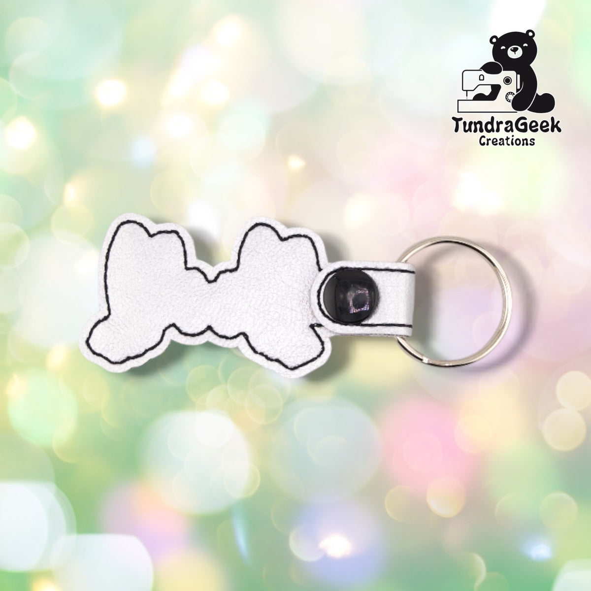 The back of the keychain, plain white vinyl with a black outline stitched around the edge. The black plastic snap and silver split ring are at the top.