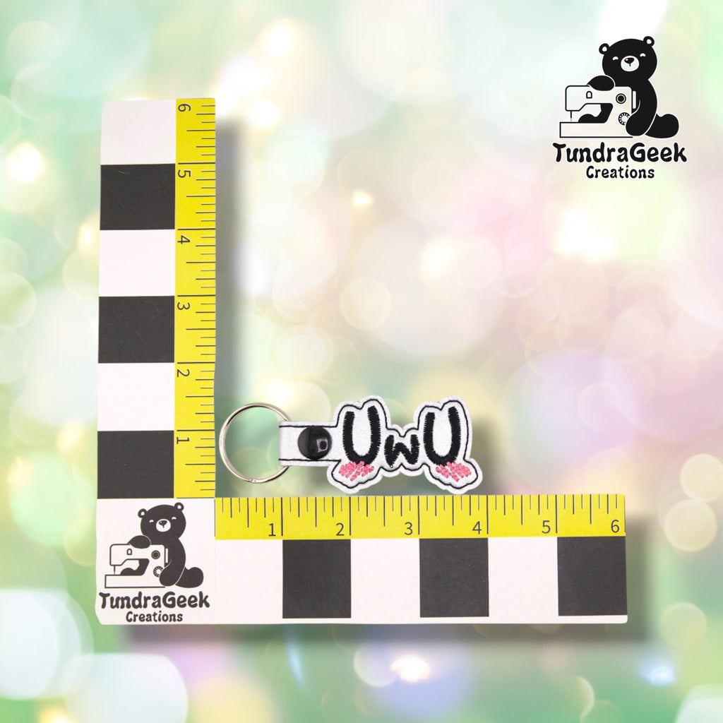 The keychain photographed against a yellow ruler marked in inches along both edges, for size reference. It measures 4 inches long by 1.5 inches tall including hardware.  ---