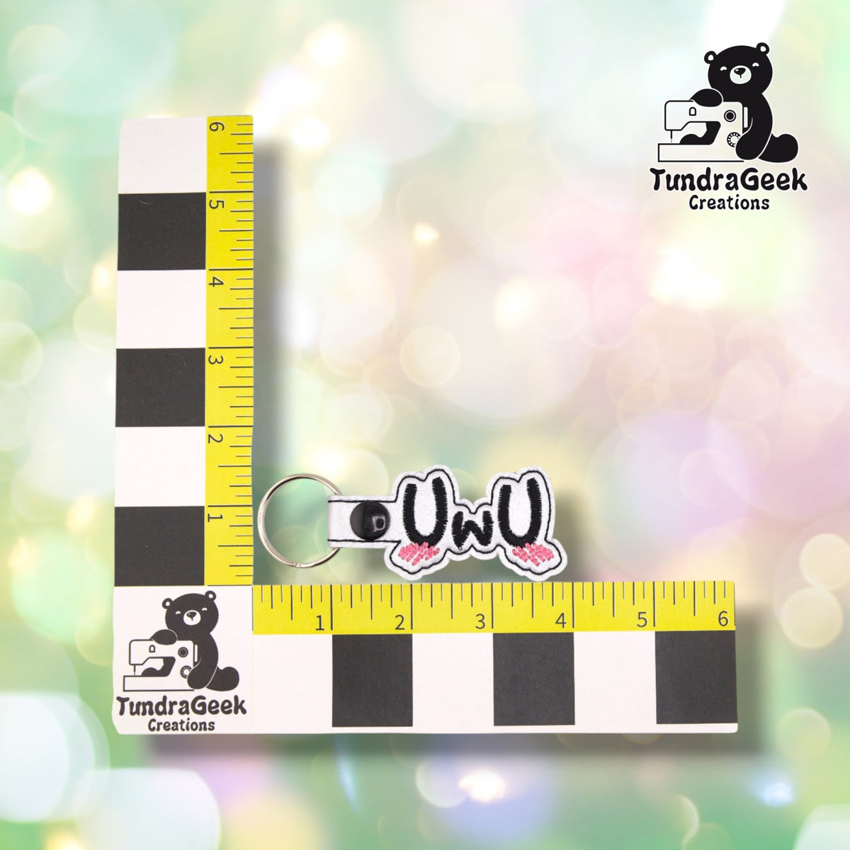 The keychain photographed against a yellow ruler marked in inches along both edges, for size reference. It measures 4 inches long by 1.5 inches tall including hardware.  ---